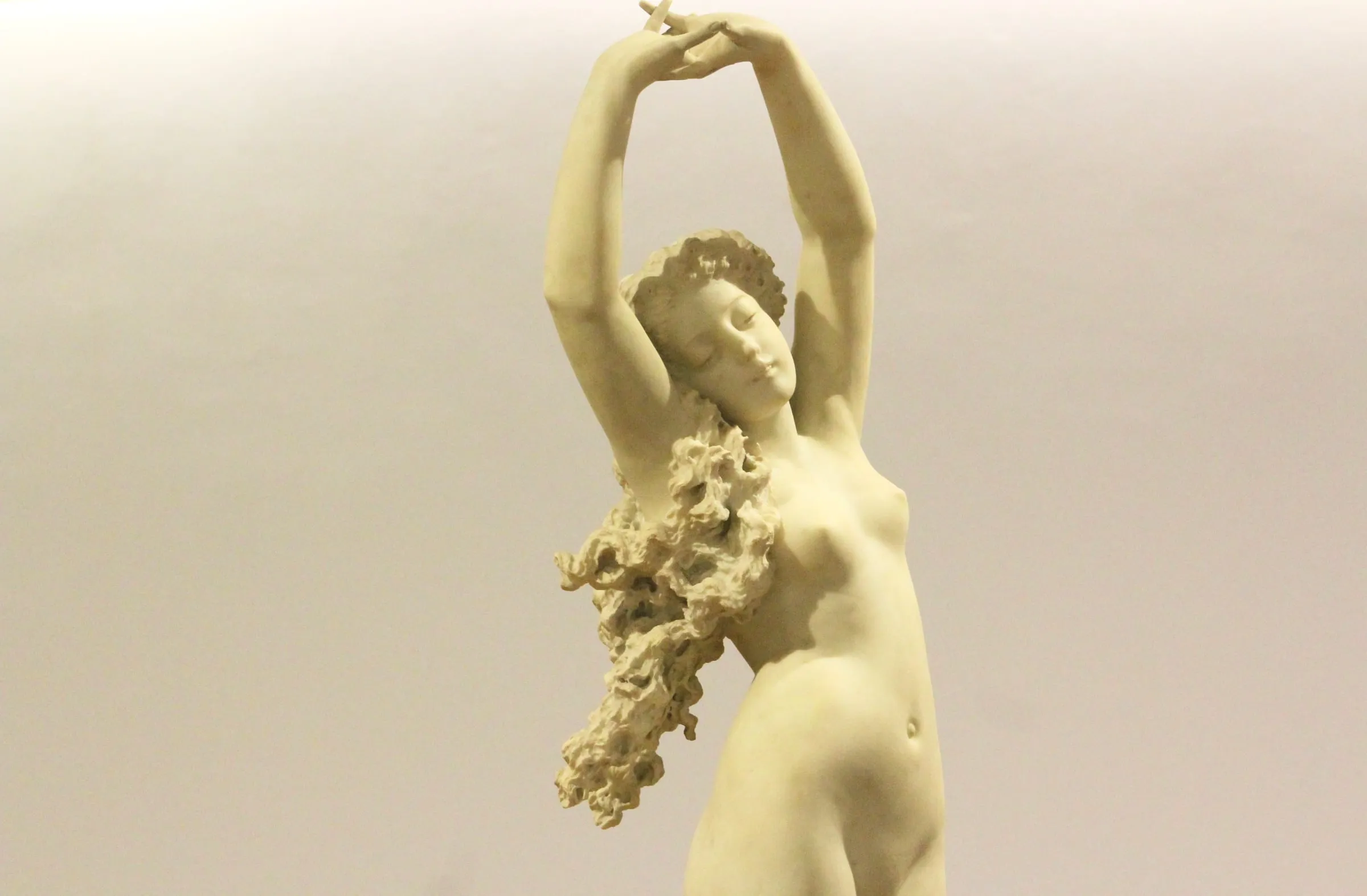 Figura femenina en mármol con los brazos alzados y flores